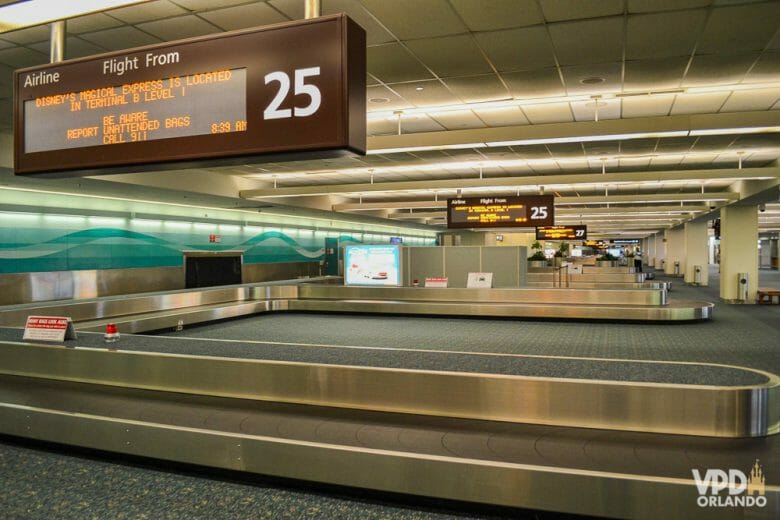 Foto da esteira de bagagem no aeroporto de Orlando, com a placa indicando as informações dos voos acima. 