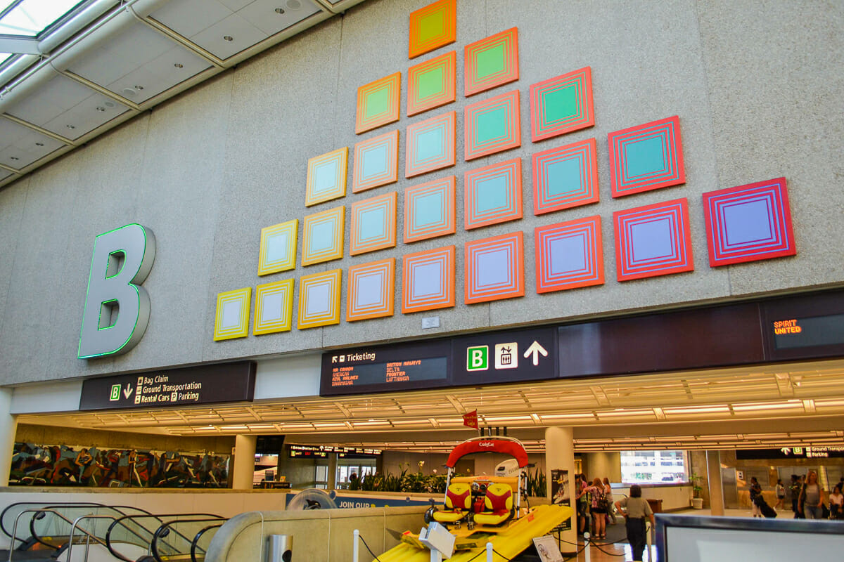 Foto do terminal B do aeroporto de Orlando, com algumas pessoas e parte das escadas rolantes visível.
