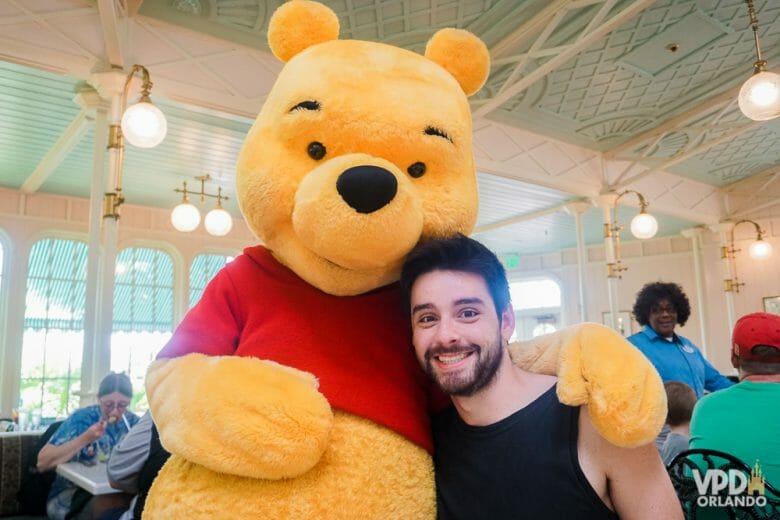 O Crystal Palace no Magic Kingdom tem café, almoço e jantar com personagens da turma do Pooh. Foto do Felipe abraçado ao Pooh na mesa do Crystal Palace. 