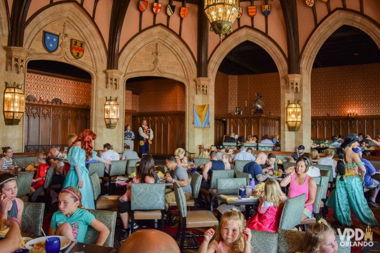 Foto do interior do restaurante Cinderella's Royal Table, com mutios visitantes sentados às mesas e as princesas Ariel e Jasmine passando entre eles para tirar fotos. 