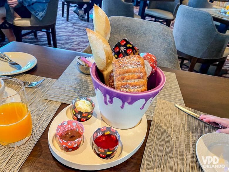 Foto da comida no Topolino's Terrace, com uma cesta de pães doces e potinhos de geleia ao lado. 