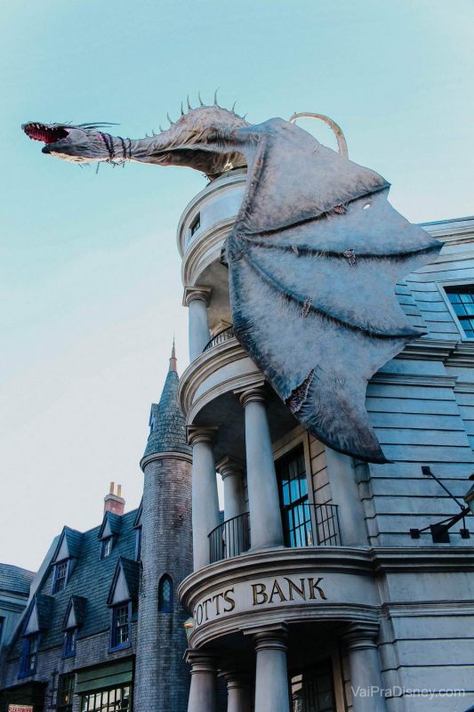 O dragão no topo do banco dos bruxos já virou ícone no parque! Foto no dragão em cima do prédio de Gringotts, no Beco Diagonal, com um céu claro ao fundo. 