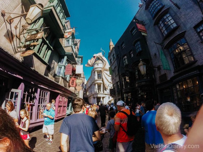 O beco diagonal é demais! A gente se sente dentro do mundo do Harry Potter. Foto do Beco Diagonal do Harry Potter no Islands of Adventure, com construções coloridas, muitos visitantes e o dragão de Gringotts ao fundo 