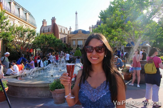 Foto da amiga da Renata, a Cati, com uma taça de champagne e o pavilhão da França ao fundo no Drinking Around the World