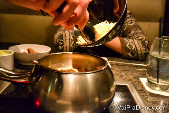 Não dá pra ver direito porque ele era muito rápido mas o garçom preparou o fondue do zero na nossa mesa. Foto do garçom jogando queijo na panelinha 