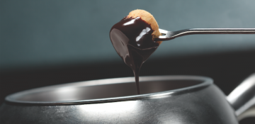 Foto de um pedaço de fruta escorrendo chocolate sobre a panela de fondue no Melting Pot