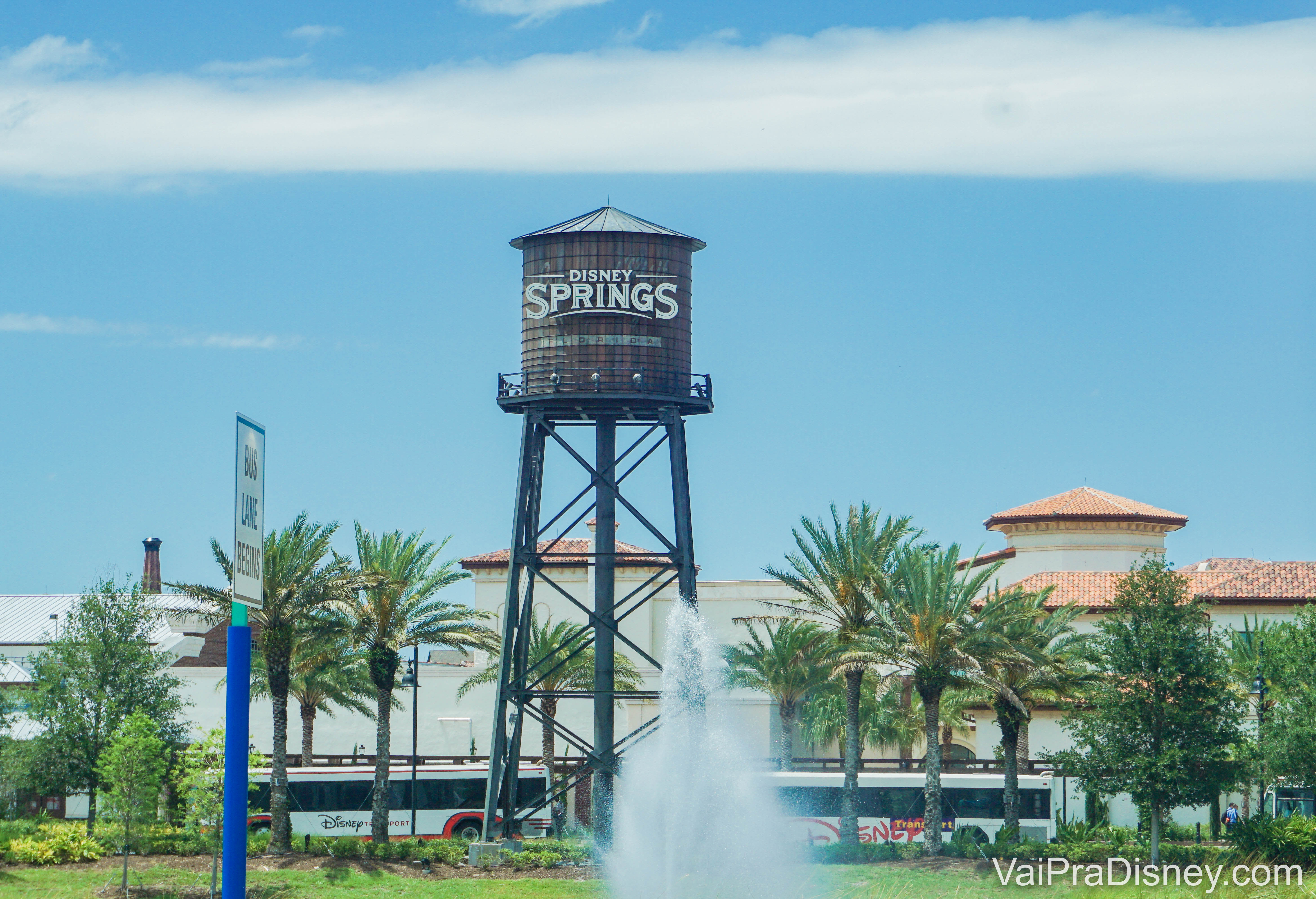 Imagem da caixa d'água com o logo de Disney Springs, com árvores ao redor e o céu azul atrás. 