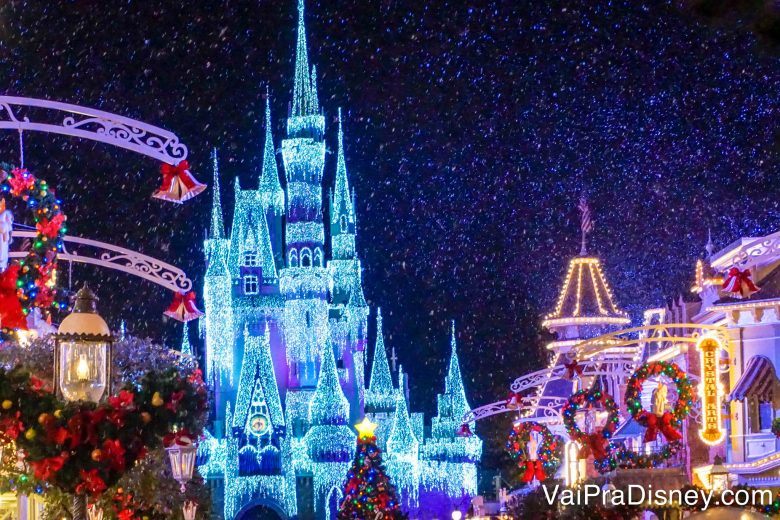 Foto da Main Street e do Castelo da Cinderela decorados e iluminados para a festa de Natal do Magic Kingdom, com neve caindo do céu 