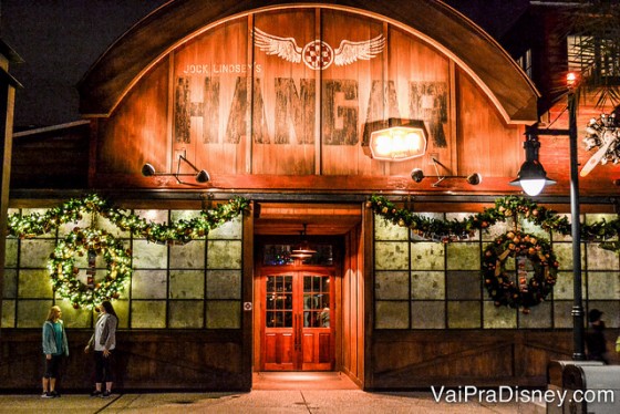 Foto da fachada do Jock Lindsey's Hangar Bar em Disney Springs, com iluminação alaranjada e estilo industrial. 