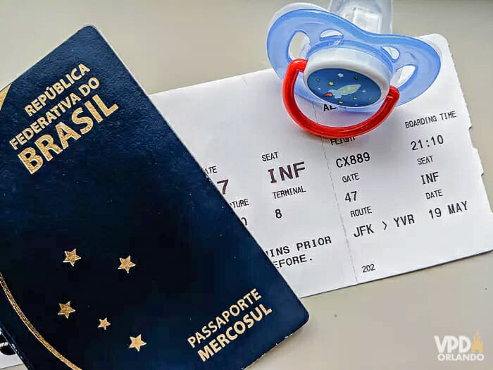 Foto de um passaporte brasileiro com uma passagem de avião embaixo e uma chupeta ao lado. 