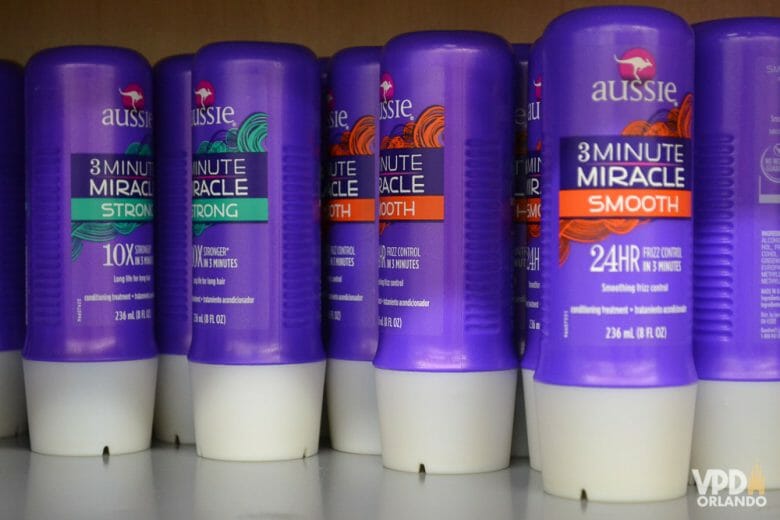 Produtos com mais de 100ml devem ir na mala despachada! Foto dos produtos de cabelo da marca Aussie na prateleira de uma loja, com a característica embalagem roxa 