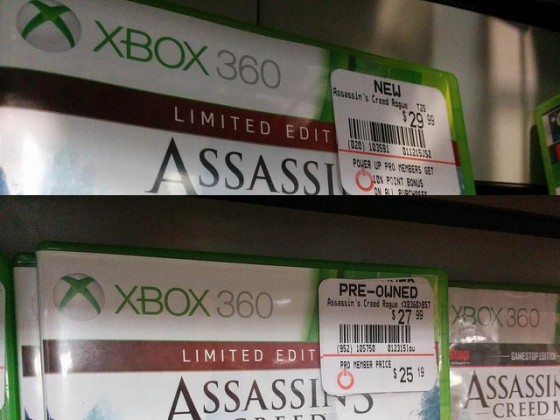 Em um lançamento, a diferença entre jogos novos e pre-owned podem não ser tão grandes. Foto do mesmo jogo, Assassin's Creed, com etiquetas de preços diferentes, um marcado como "new" e outro "pre-owned" 