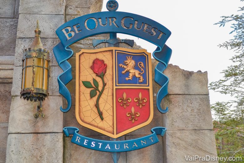 Foto da placa na entrada do restaurante Be our Guest, no Magic Kingdom. Ela imita um brasão medieval com uma rosa, um leão e espadas. 