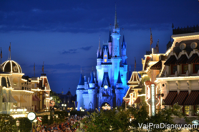 Foto do castelo da Cinderela do Magic Kingdom iluminado em azul, com o céu noturno ao fundo e as luzes da Main Street acesas 