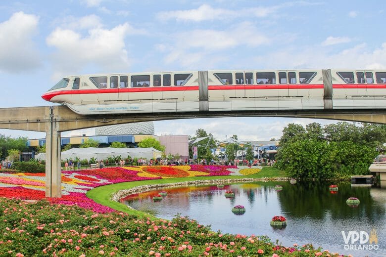 Foto do Monorail passando sobre o Epcot, na ponte em cima do lago, rodeada por flores e o céu azul ao fundo. Usada para ilustrar o post de wallpapers de celular