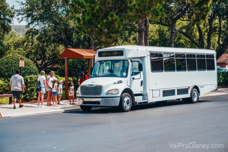 Ponto de ônibus com hóspedes embarcando em um mini ônibus branco, com destino aos parques temáticos.