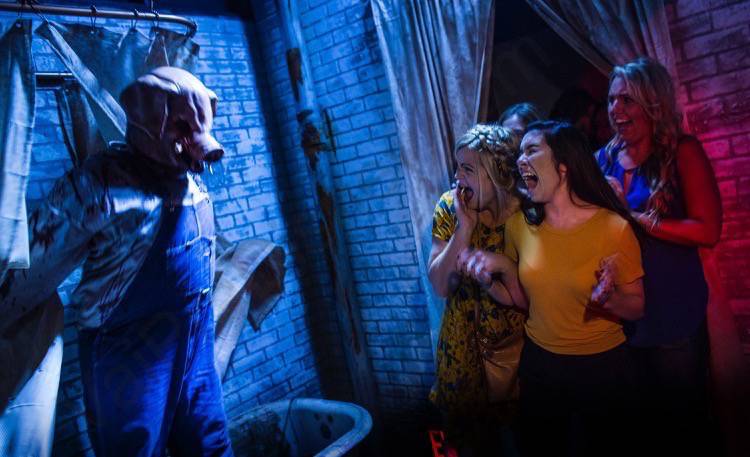 Foto da Halloween Horror Nights da Universal, uma das festas mais famosas de Orlando. A imagem mostra três visitantes gritando, após levarem um susto com um personagem com máscara de porco. 