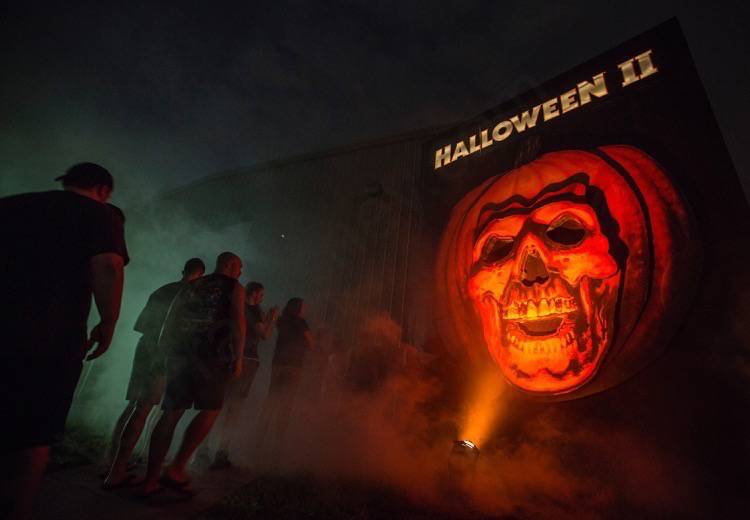 Labirinto do filme Halloween 2 na Halloween Horror Nights da Universal. A entrada mostra uma abóbora gigante com rosto de caveira, e visitantes enfileirados na porta. 