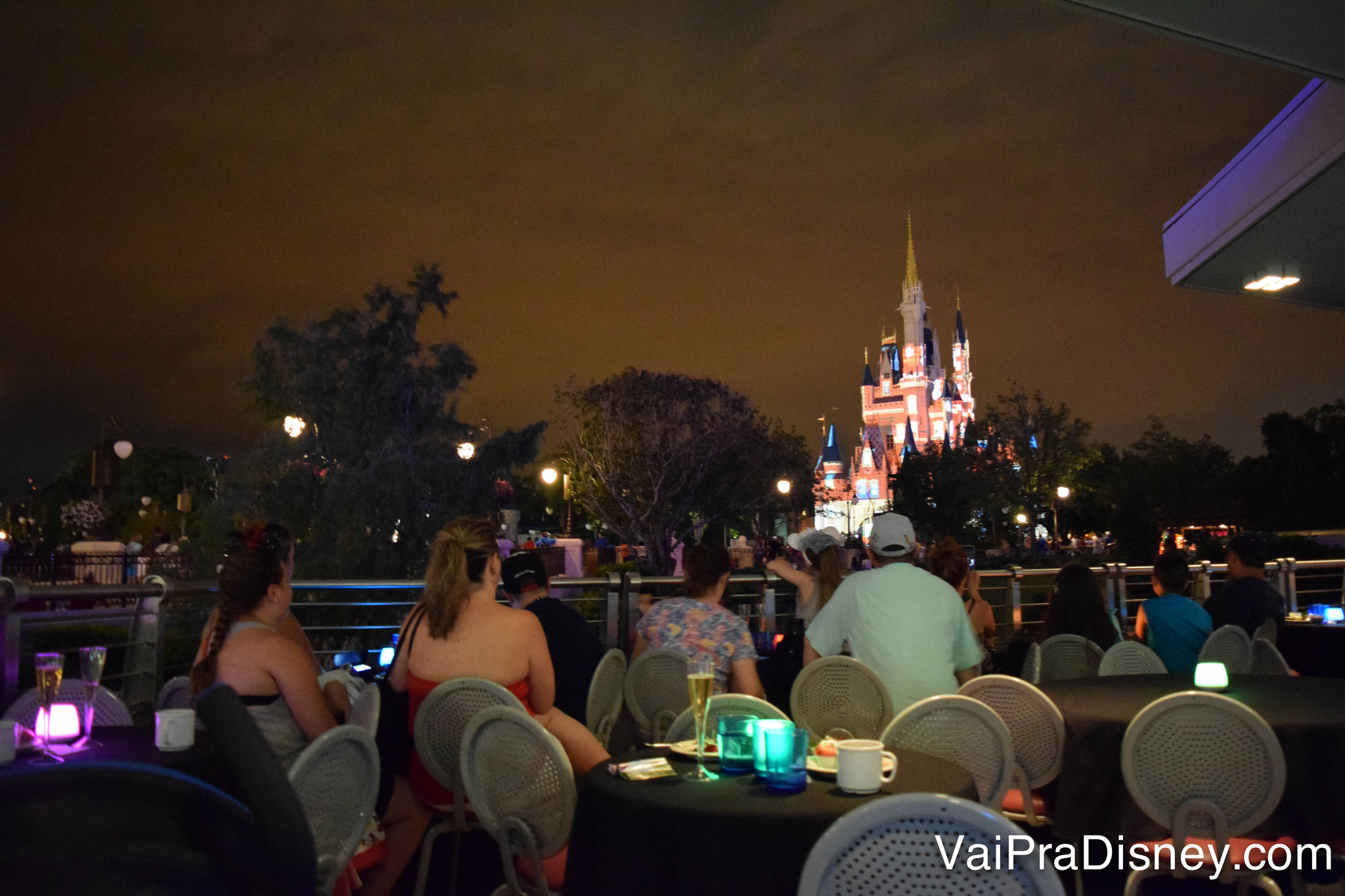 Foto das mesas na área VIP, com o castelo iluminado bem à frente 