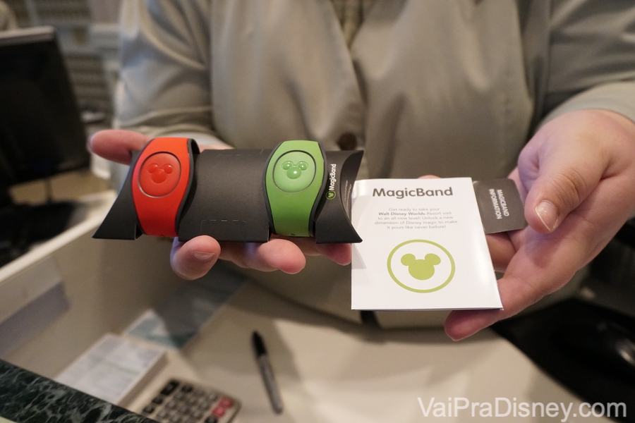 Todos os hóspedes de hotéis da Disney recebem as MagicBands no check in. Foto de uma mão segurando duas MagicBands dos hotéis da Disney, uma laranja e outra verde.