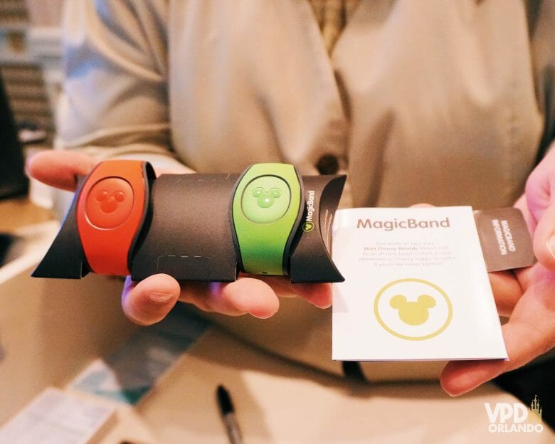 oto de uma mão segurando duas MagicBands dos hotéis da Disney, uma laranja e outra verde.