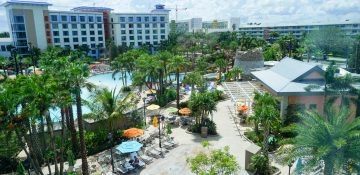 Foto da área externa do Loews Sapphire Falls Resort, mostrando o prédio branco com detalhes em azul e parte da área da piscina, com palmeiras em volta