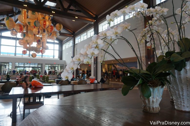 Outra foto do lobby mostrando flores sobre a mesa e o lustre de bolas de praia 