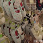 Foto de diversos sapatinhos de bebê à venda em uma loja, em sua maioria em cores claras.