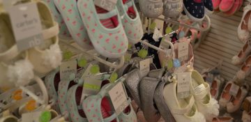 Foto de diversos sapatinhos de bebê à venda em uma loja, em sua maioria em cores claras.