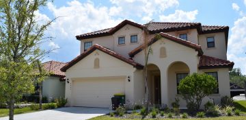 Foto de uma casa alugada em Orlando. Ela é pintada de cor clara, quase branca, tem um gramado verde à frente e o céu azul é visível atrás.