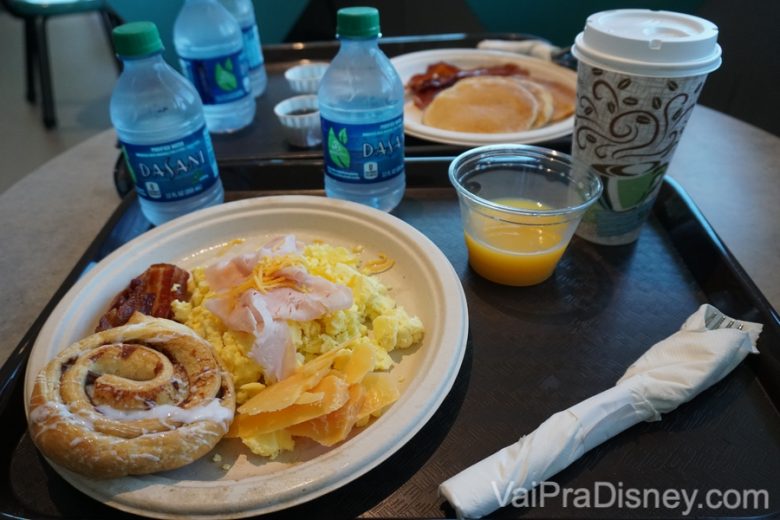 Foto do café-da-manhã servido no Early Morning Magic, com café, suco de laranja, água, ovos mexidos, pão doce e bacon. 