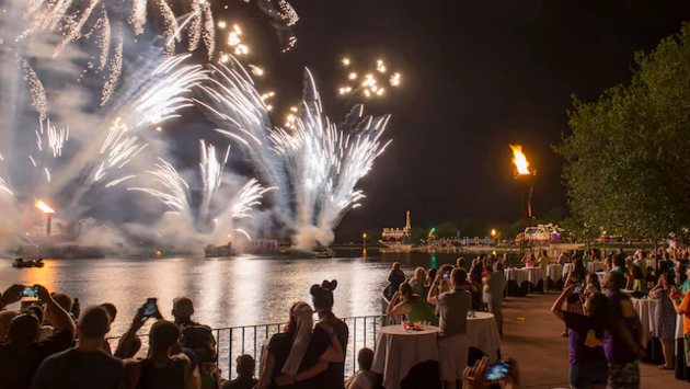 Foto da área VIP do IllumiNations Dessert Party, com várias mesas, e os fogos sobre o lago mais ao fundo da foto 