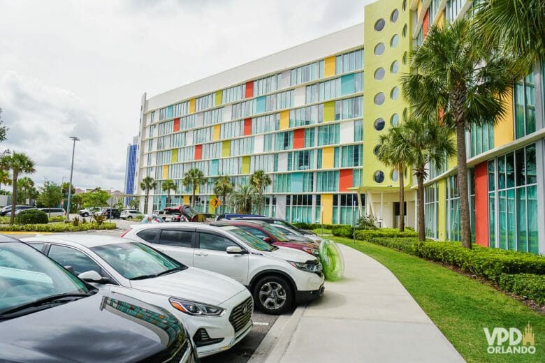 Muitos hotéis cobram uma diária para usar o estacionamento, como os da Disney e da Universal. Foto do estacionamento do Cabana Bay, com carros enfileirados e o prédio colorido ao fundo. 