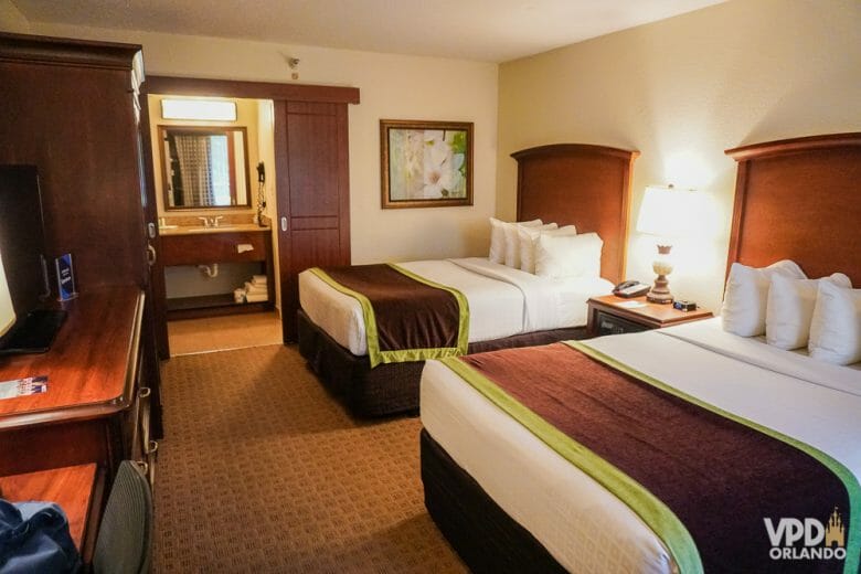 Um bom exemplo de hotel econômico e com segurança em Orlando é o Clarion Inn Lake Buena Vista. Foto do quarto do Clarion Inn Lake Buena Vista, com duas camas de casal e a pia do banheiro à vista no fundo. 