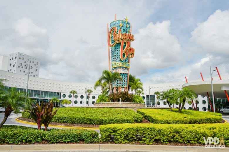 Entrada do hotel Cabana Bay, da Universal. Na foto é possível ver o totem central que tem o nome do hotel, letras laranjas em um fundo azul-turquesa. 