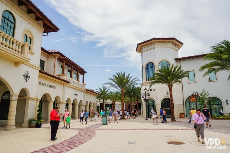 O Disney Springs é um ótimo lugar pra trocar o e-ticket e ainda emendar num passeio super gostoso. O Ticket Center fica atrás da loja da Zara. Imagem do centro de Disney Springs, que parece uma praça, com árvores e lojas pintadas de cores claras. 