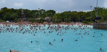 Imagem do Blizzard Beach, parque aquático da Disney, durante o verão. É possível ver a piscina de ondas cheia de visitantes, e o céu azul e as árvores ao fundo.