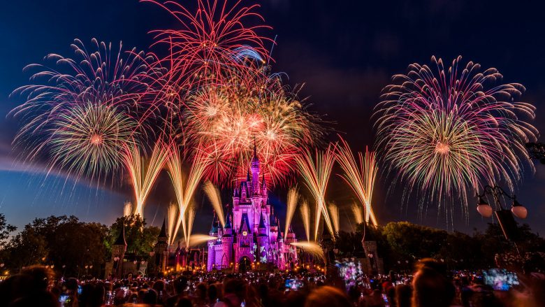 Foto do show de fogos especial de 4 de julho no Magic Kingdom, com o castelo iluminado em roxo e vermelho. 