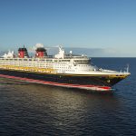 Imagem do navio de cruzeiro da Disney em alto mar. Ele tem detalhes em azul marinho, vermelho, branco e amarelo