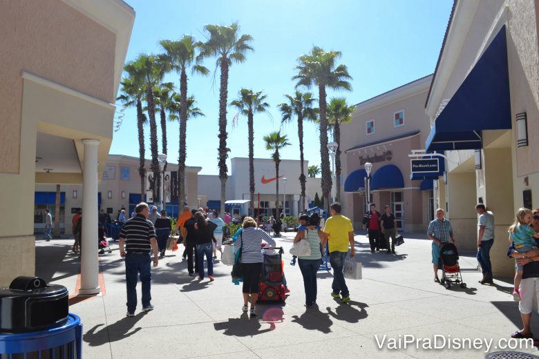 Outlets que a gente tanto ama! Foto da área aberta de um outlet, com visitantes passeando e o céu azul ao fundo 