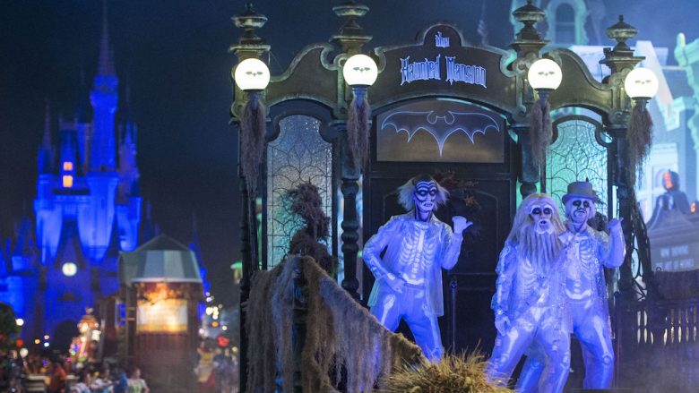 Imagem da parada especial de Halloween. Há três pessoas vestidas de esqueleto sobre o carro, iluminados por uma luz azul, e o castelo da Cinderela está ao fundo 