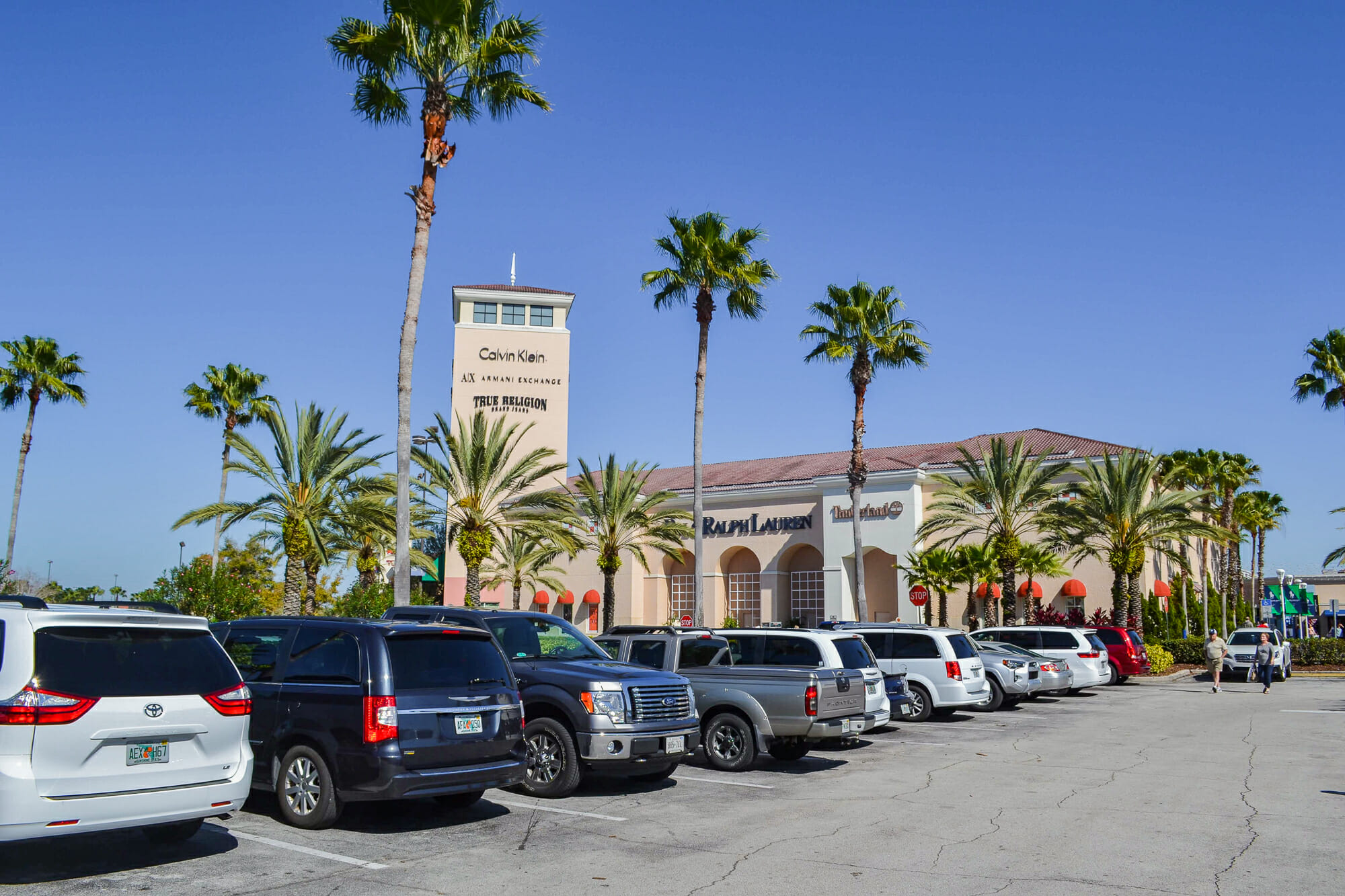 Imagem do estacionamento do Premium Outlet em Orlando, com carros enfileirados e o céu azul ao fundo.