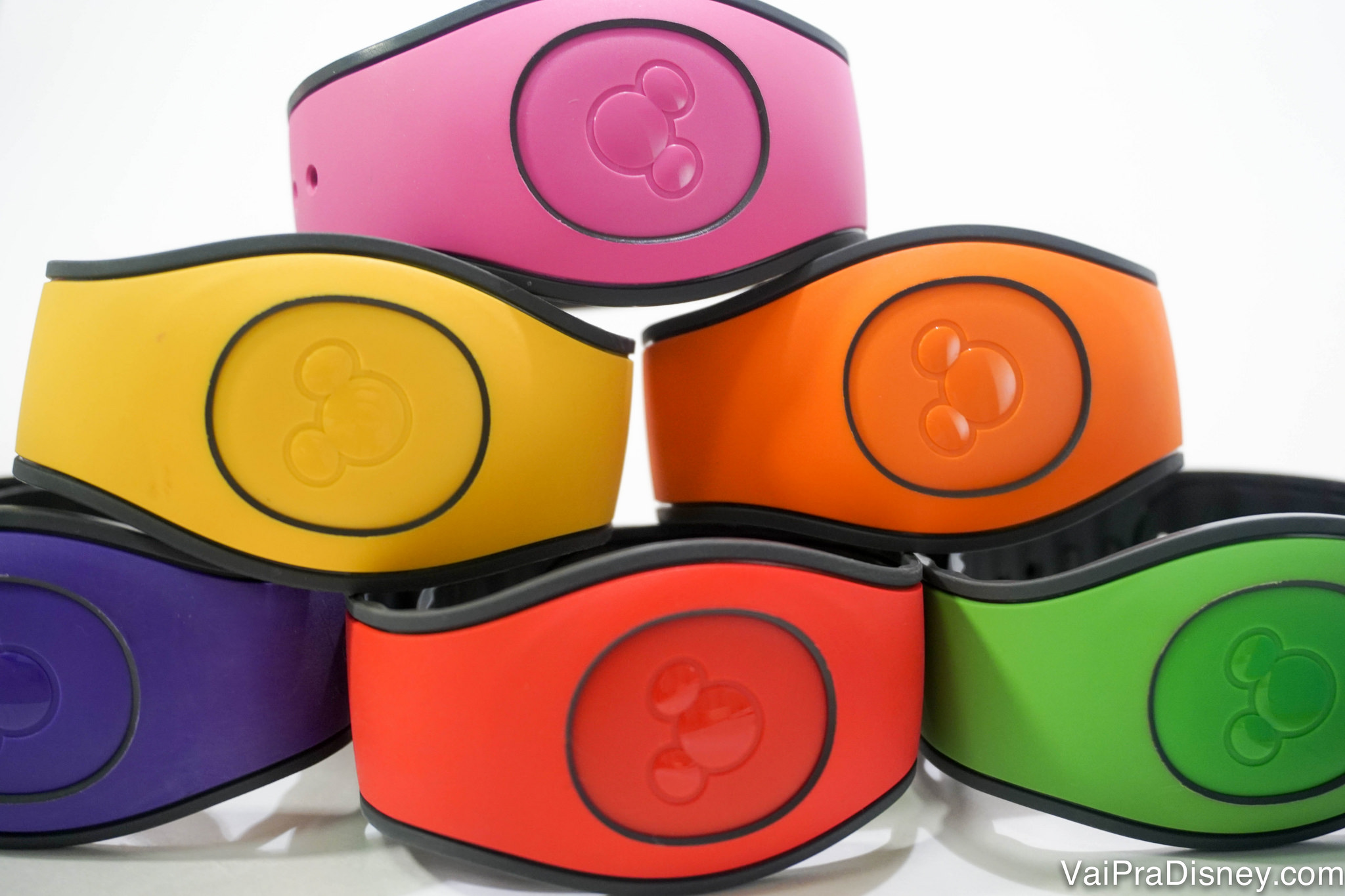 As famosas magicbands da Disney que todos querem usar. Foto de uma pilha com seis MagicBands da Disney nas cores rosa, amarela, laranja, azul, vermelha e verde. 