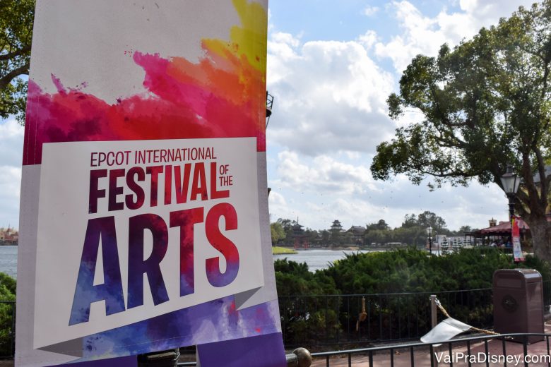 Foto do cartaz do Disney's Festival of the Arts no Epcot, pintado em aquarela em várias cores, com o parque ao fundo. 