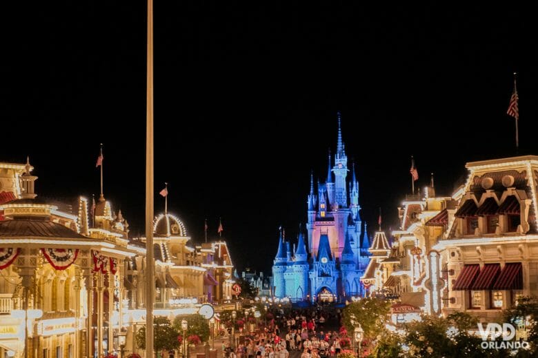 Os parques podem ficar mais cheios com o Spring Break! Foto do Castelo da Cinderela iluminado em azul e a Main Street do Magic Kingdom, cheia de pessoas e também iluminada. 