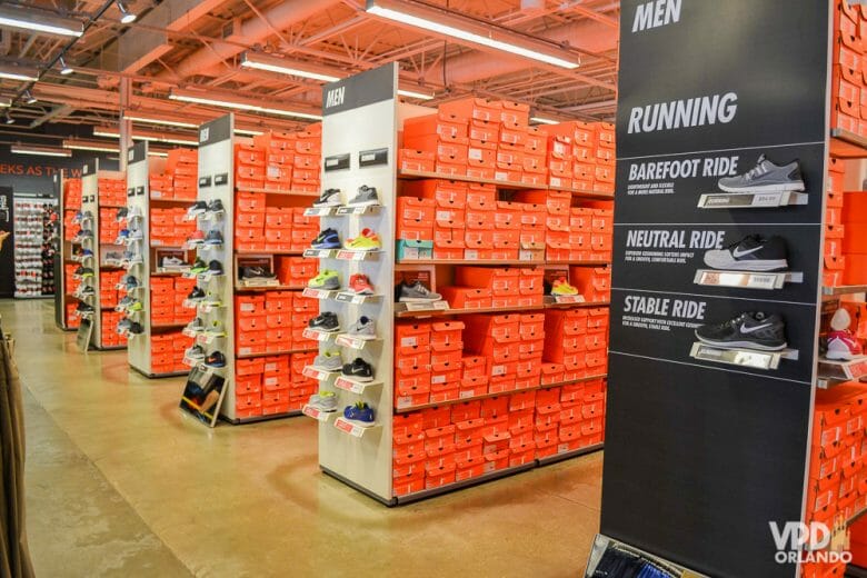 Mesmo com menos promoções, os cupons e descontos continuam nos outlets em Abril. Foto do outlet da Nike, onde é possível ver corredores repletos de caixas alaranjadas, e alguns tênis em exibição. 