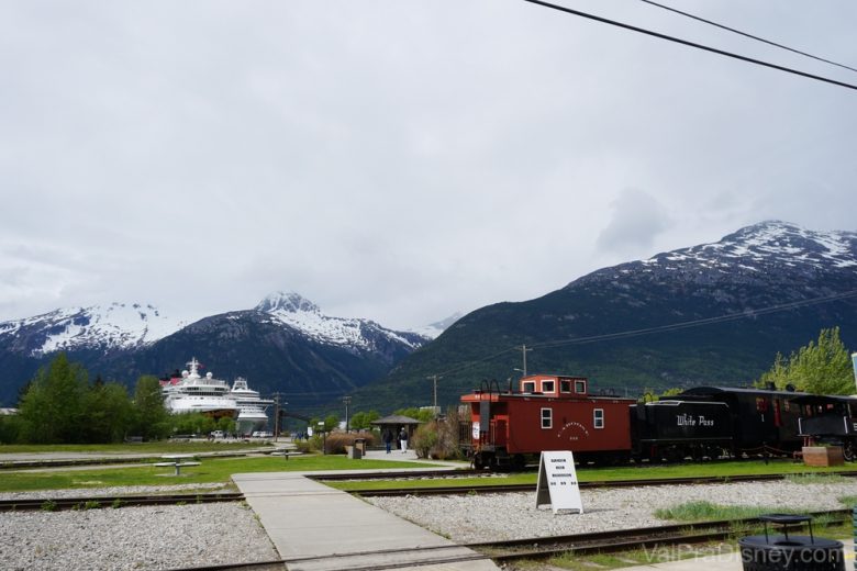 Foto do trem na cidade de Skagway, com o navio da Disney ao fundo 