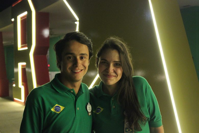 Foto da Bia e do Henrique trabalhando na Disney, no All Star, com uniformes verdes  