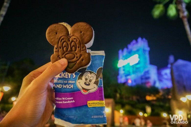 Foto de um sanduíche de sorvete em formato de Mickey, com a Tower of Terror iluminada ao fundo. 