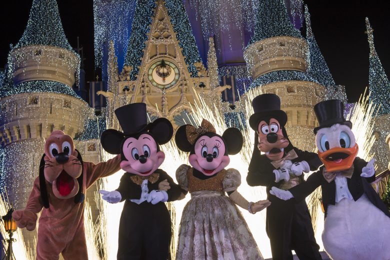 Show de ano novo no Magic Kingdom. Imagem: Divulgação Disney. Foto do show de Ano Novo do Magic Kingdom, mostrando Pluto, Mickey, Minnie, Pateta e Donald em roupas de festa em frente ao castelo da Cinderela iluminado.